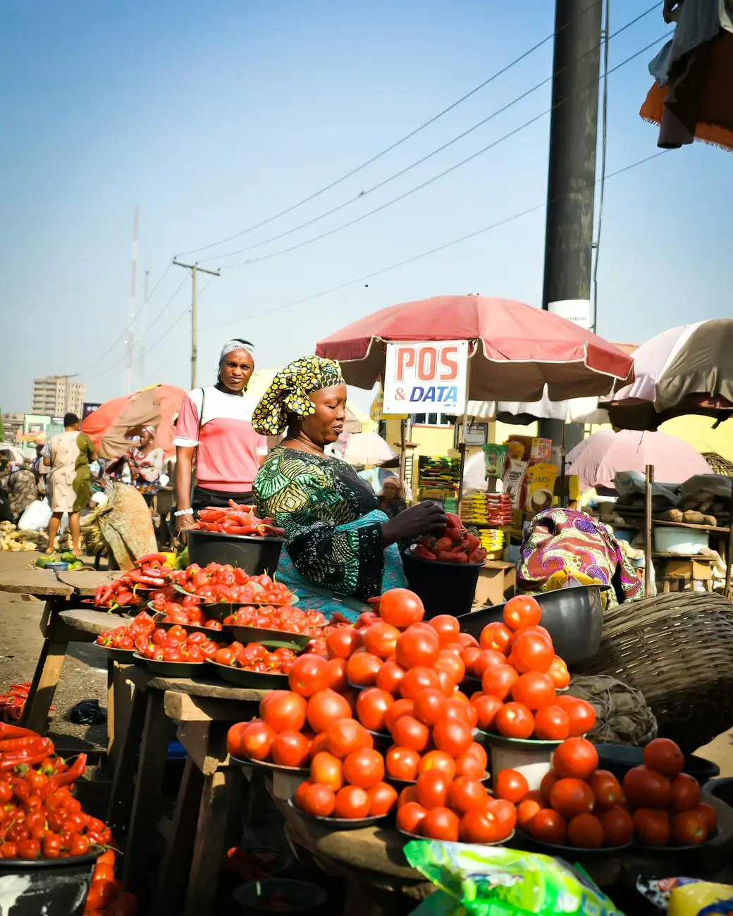 A trader at a busy produce market, under a mobile-money POS umbrella